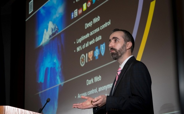 Man in a suit in front of a presentation slide on artificial intelligence tools for analyzing surface, deep, and dark-web data.